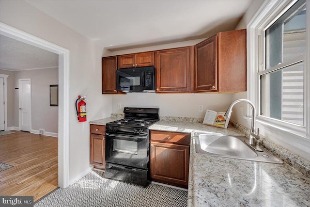 kitchen with light wood-style flooring, brown cabinets, light stone countertops, black appliances, and a sink