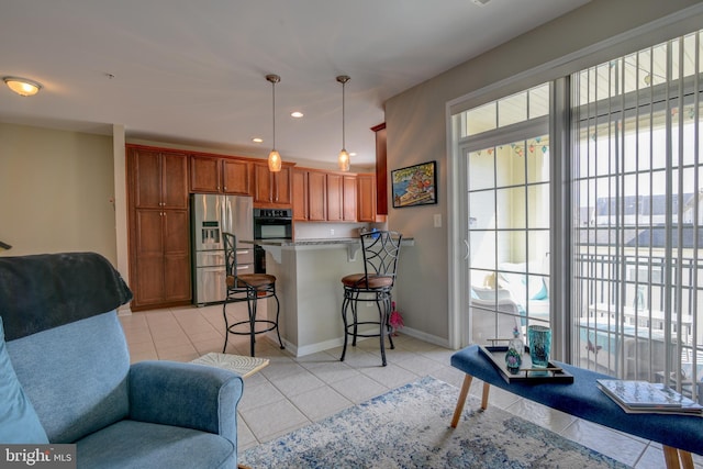 kitchen featuring light tile patterned flooring, a peninsula, a breakfast bar, hanging light fixtures, and stainless steel fridge