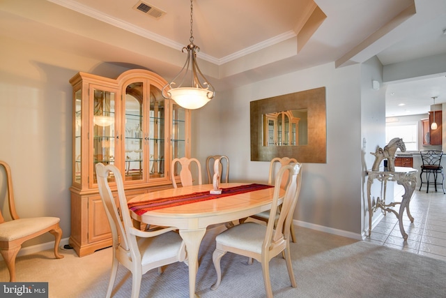 dining room with a tray ceiling, crown molding, visible vents, light carpet, and baseboards