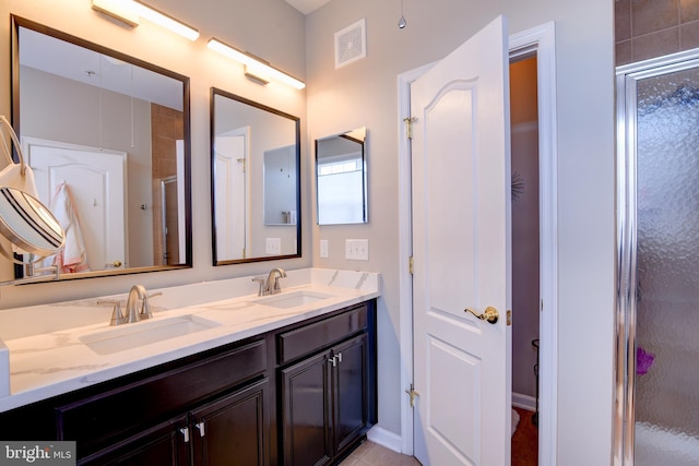 full bath featuring double vanity, an enclosed shower, visible vents, and a sink