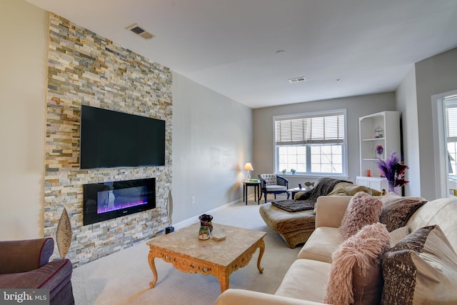 living area featuring baseboards, visible vents, carpet flooring, and a stone fireplace