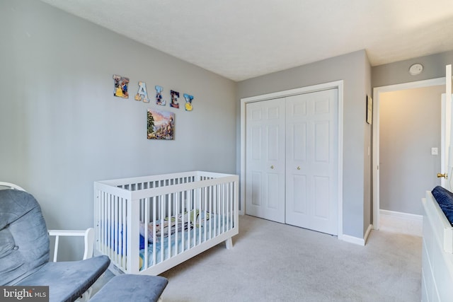 bedroom featuring a nursery area, a closet, light carpet, and baseboards