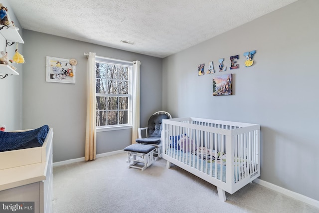 bedroom with a textured ceiling, carpet floors, visible vents, baseboards, and a nursery area