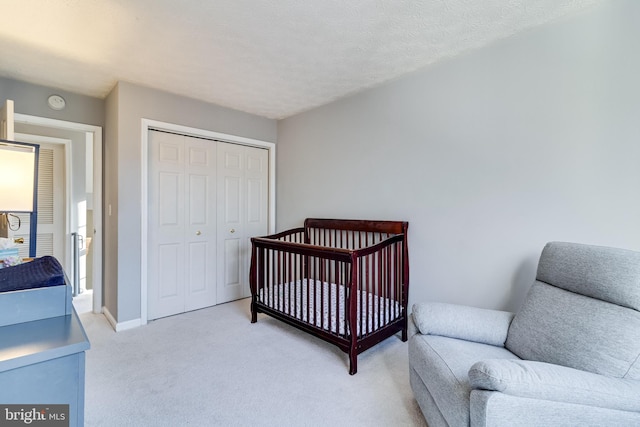 bedroom with a closet, light carpet, a textured ceiling, and baseboards