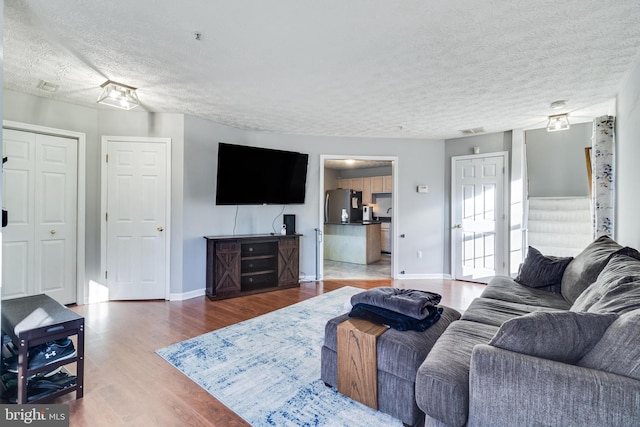 living room with a textured ceiling, wood finished floors, visible vents, and baseboards