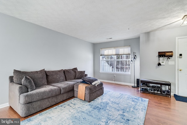 living room with a textured ceiling, baseboards, and wood finished floors