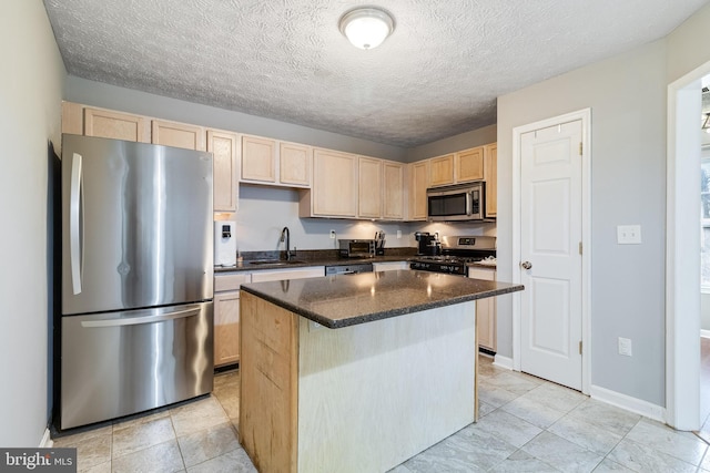 kitchen featuring light brown cabinetry, appliances with stainless steel finishes, a kitchen island, a sink, and baseboards