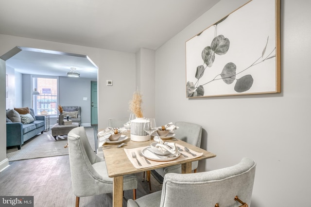 dining room with arched walkways, baseboards, and wood finished floors