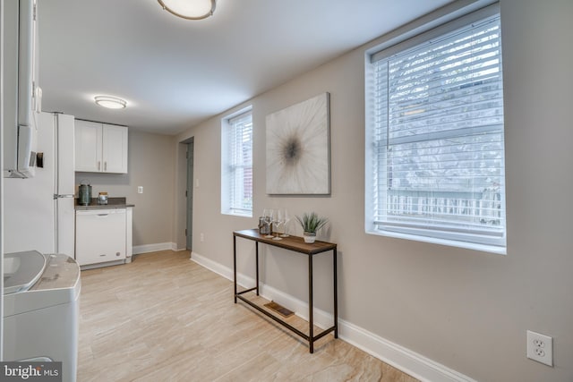 kitchen featuring dark countertops, baseboards, white dishwasher, and white cabinetry