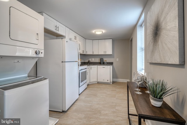 kitchen featuring dark countertops, white appliances, white cabinets, and stacked washing maching and dryer