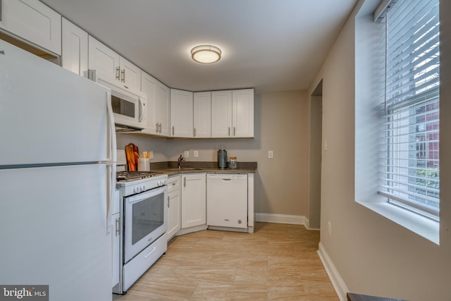 kitchen with white appliances, baseboards, dark countertops, white cabinetry, and a sink