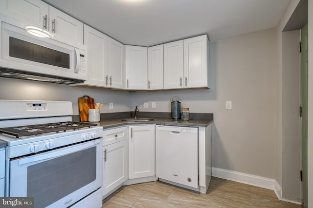 kitchen with dark countertops, white appliances, white cabinetry, and a sink