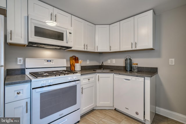 kitchen featuring dark countertops, white appliances, white cabinetry, and a sink