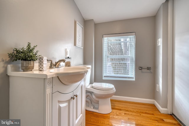 bathroom with toilet, wood finished floors, vanity, and baseboards