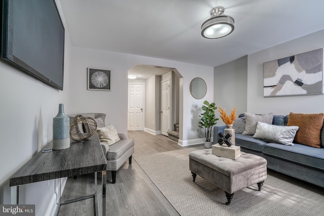 living area featuring arched walkways, baseboards, and light wood finished floors