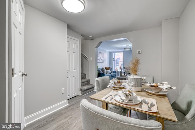 dining area with baseboards, stairs, arched walkways, and wood finished floors