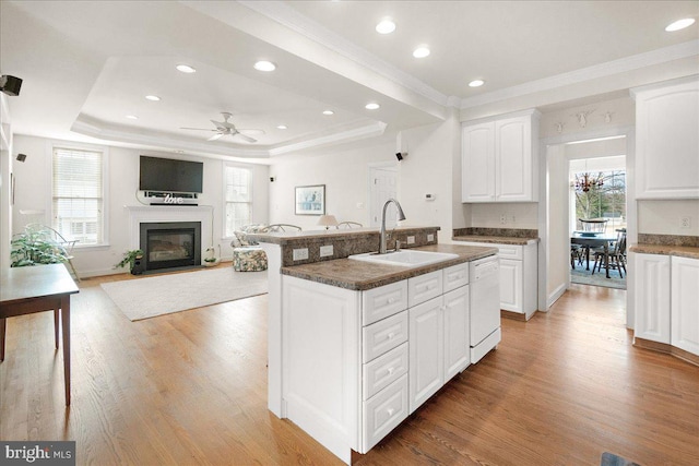 kitchen featuring a raised ceiling, light wood-style flooring, a fireplace with flush hearth, white dishwasher, and a sink