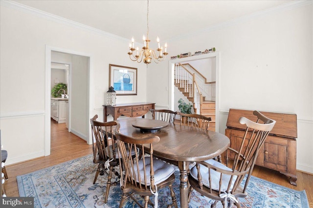 dining space featuring light wood-style floors, baseboards, ornamental molding, and a notable chandelier