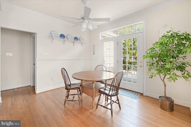 dining area featuring wainscoting, ornamental molding, light wood-type flooring, and a ceiling fan