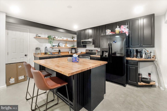 kitchen featuring open shelves, wooden counters, appliances with stainless steel finishes, a sink, and a kitchen breakfast bar