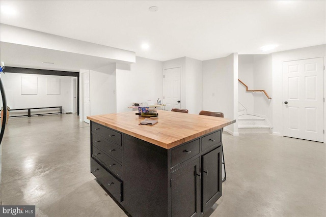 kitchen featuring concrete flooring, butcher block countertops, baseboards, and dark cabinets