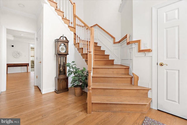 stairway with ornamental molding, a high ceiling, baseboards, and wood finished floors