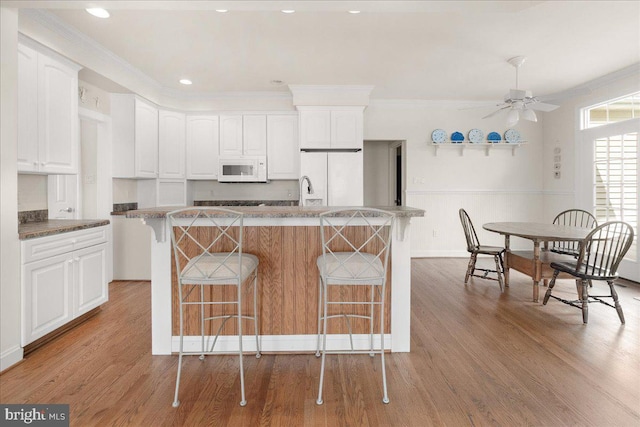 kitchen with white appliances, white cabinetry, and a kitchen bar