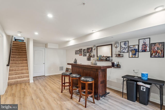 bar with bar, light wood-style flooring, visible vents, baseboards, and stairs