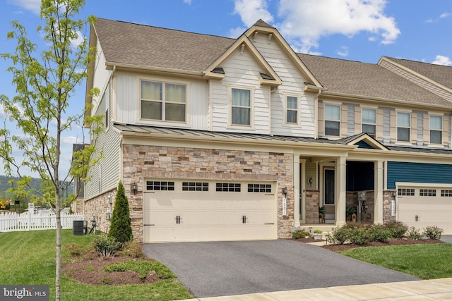 view of front of property with cooling unit, stone siding, a standing seam roof, an attached garage, and fence