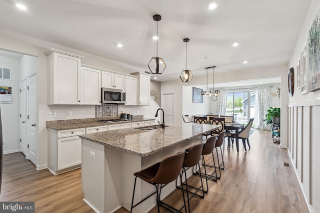 kitchen with light wood-type flooring, stainless steel appliances, light stone countertops, and a sink