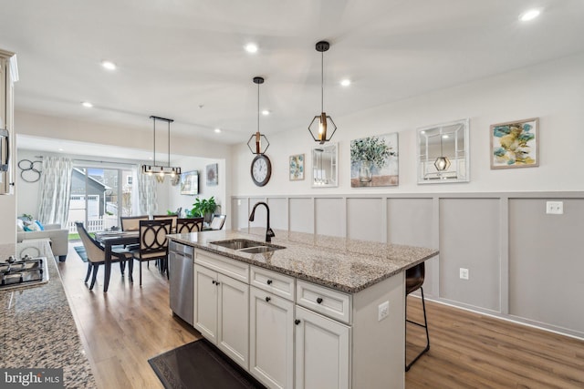 kitchen with light stone countertops, stainless steel dishwasher, light wood-style flooring, white cabinets, and a sink