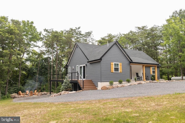 exterior space with a front yard, roof with shingles, a wooden deck, and stairs