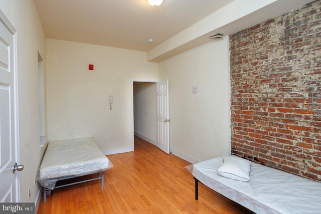 living area featuring brick wall, light wood-type flooring, and baseboards