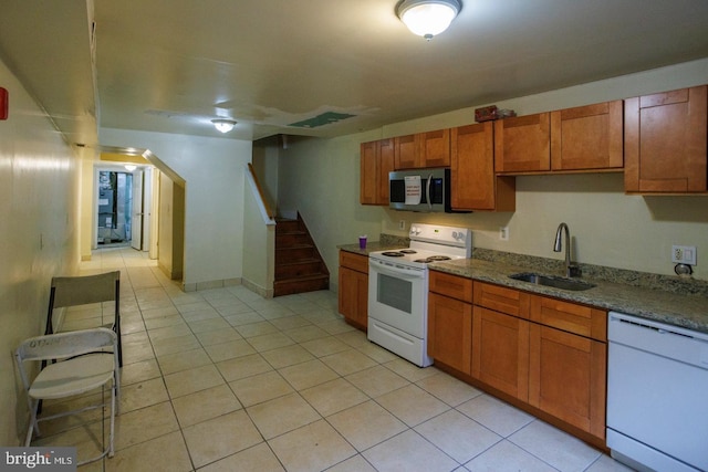 kitchen with stone counters, light tile patterned flooring, white appliances, a sink, and brown cabinetry