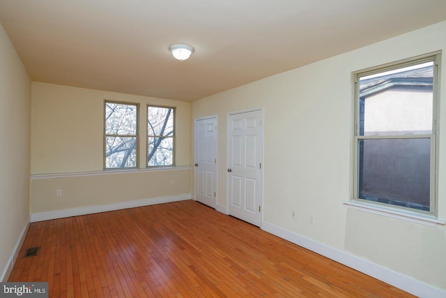 spare room with wood finished floors, visible vents, and baseboards