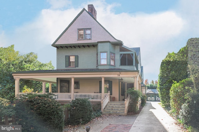 victorian house with a garage, a porch, and a chimney