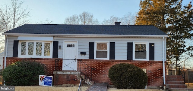 bungalow-style house featuring brick siding, a chimney, and a shingled roof