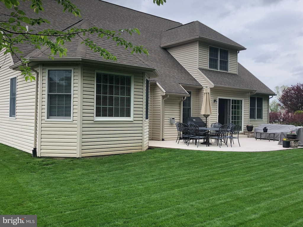 rear view of house featuring roof with shingles, a lawn, and a patio area