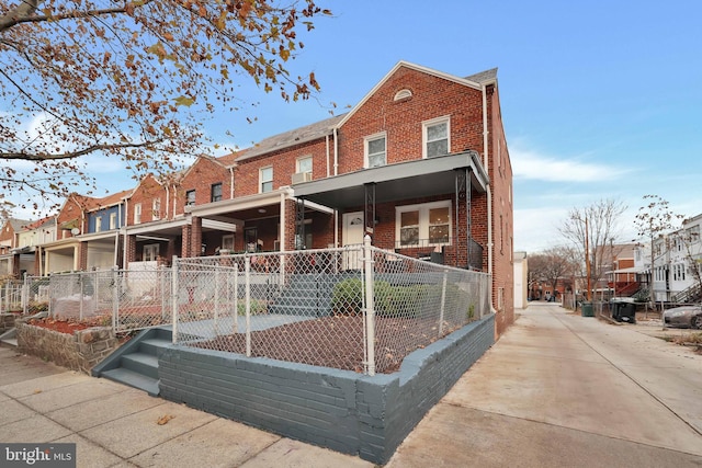 view of property featuring brick siding, a fenced front yard, a porch, and a residential view