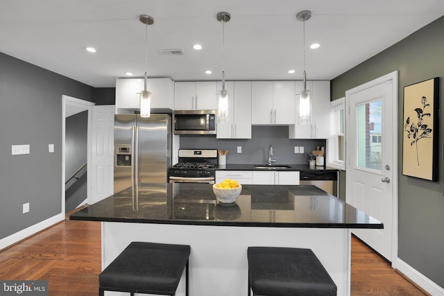 kitchen with stainless steel appliances, a kitchen island, a sink, white cabinetry, and decorative light fixtures