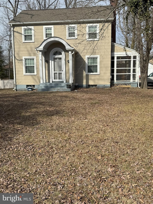 colonial home with a chimney, a front yard, and a sunroom