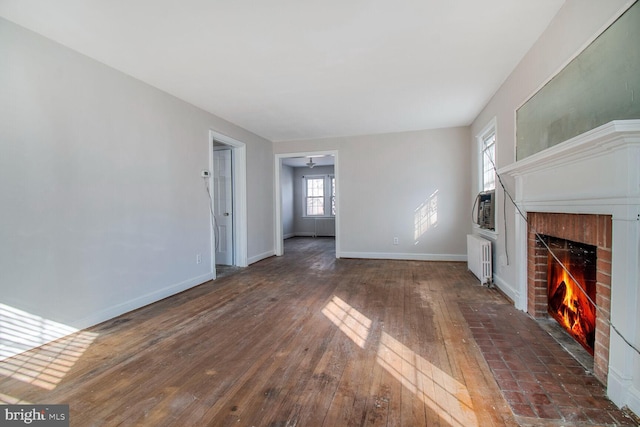 unfurnished living room featuring radiator, a fireplace, baseboards, and dark wood-style flooring