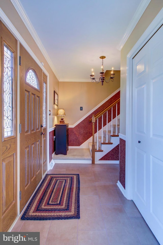 tiled entryway featuring ornamental molding, a notable chandelier, and stairs