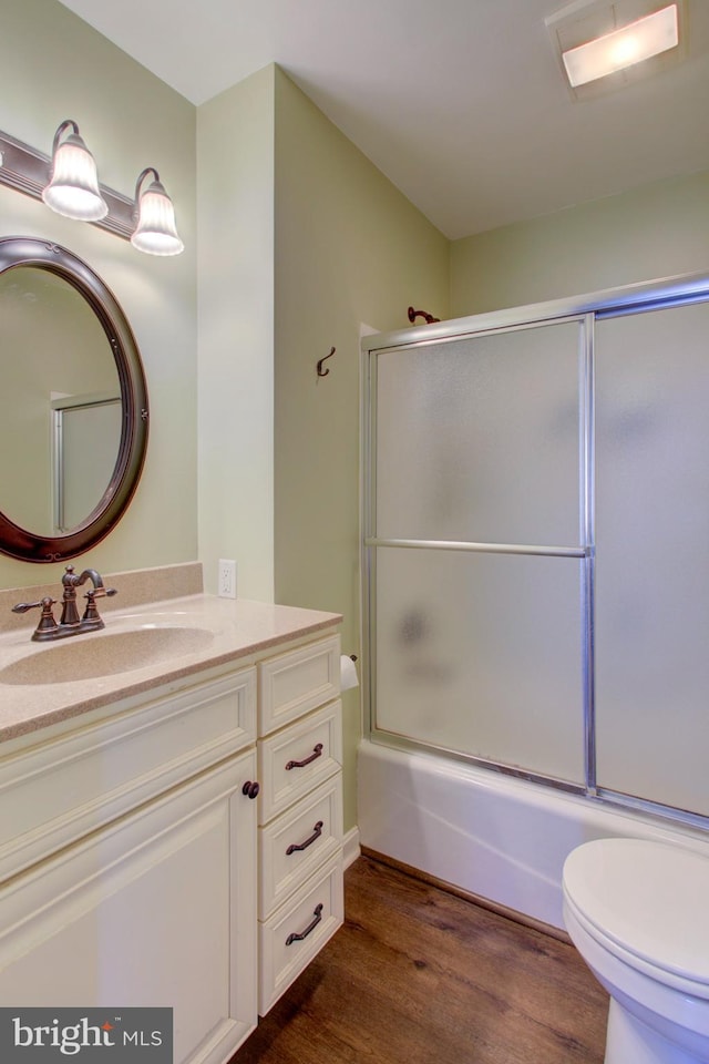 bathroom featuring toilet, enclosed tub / shower combo, wood finished floors, and vanity