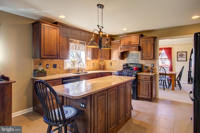 kitchen featuring light stone counters, decorative light fixtures, a kitchen island, a sink, and black appliances