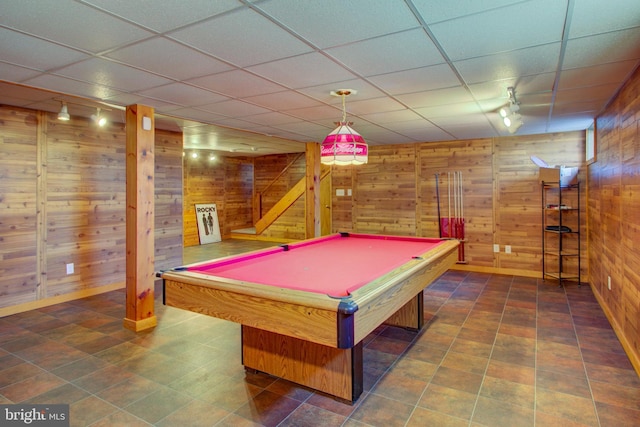 recreation room with track lighting, a drop ceiling, and wooden walls