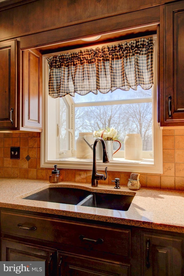 kitchen with dark brown cabinetry, light stone countertops, decorative backsplash, and a sink