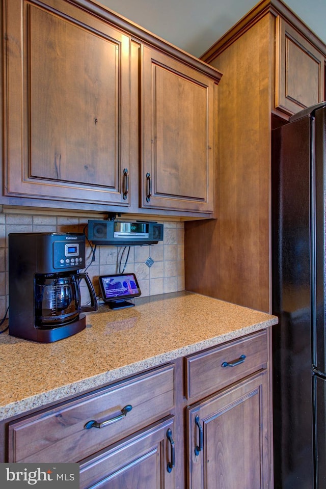 kitchen featuring light stone countertops, brown cabinets, backsplash, and freestanding refrigerator