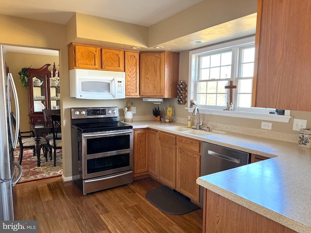 kitchen with appliances with stainless steel finishes, light countertops, a sink, and dark wood-type flooring