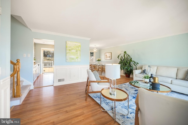 living room featuring stairs, visible vents, light wood-style flooring, and crown molding